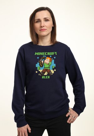 Granatowy sweter z pikselowym bohaterem Minecrafta, Alexem, trzymającym kilof. Tekst 'MINECRAFT' i 'ALEX' w kolorze zielonym. Miękka faktura.