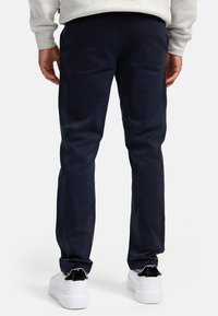 Pantalones de algodón azul marino con corte recto, que presentan bolsillos traseros y una textura suave, combinados con zapatillas blancas.