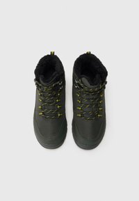 Vihreät vaelluskengät, joissa on pehmeä musta tekoturkisvuori, keltaiset nauhat ja metalliset silmukat. Karkea pohja ja sileä päällinen.