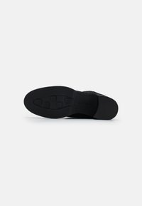 Suela de zapato negra con una superficie de goma texturizada, que presenta patrones cuadrados y una sección del talón suave, diseñada para un buen agarre y durabilidad.