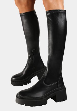 Bottes noires montantes en cuir lisse avec un talon épais, zipper latéral et semelle texturée pour une meilleure adhérence.