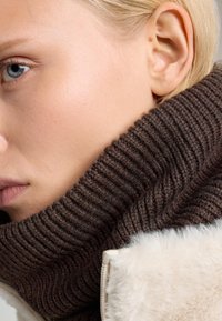 Brun ribbet strik turtleneckkrave med en blød tekstur, suppleret af en fyldig hvid kant ved jakken.