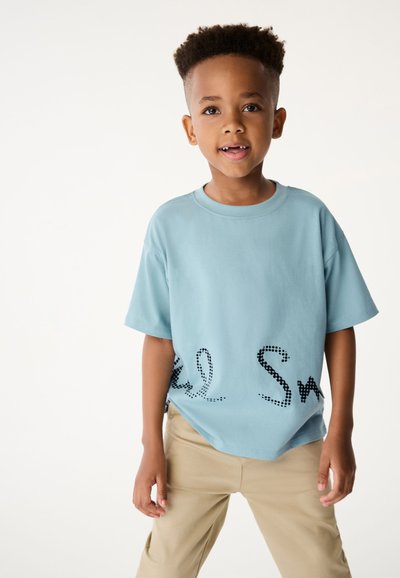 Gaiši zils īsām piedurknēm T-krekls ar melniem punktiņiem apakšā. Audums izskatās gluds; brīvs piegriezums ar noapaļotu kakla izgriezumu.