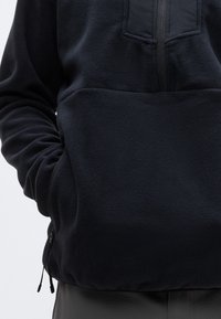 Μαύρο φλις πουλόβερ με φερμουάρ σε θήκη στο στήθος, μαλακή υφή, ελαστικές μανσέτες και στρίφωμα με κορδόνι για ρυθμιζόμενη εφαρμογή.