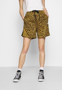 Pantaloni corti con stampa leopardata gialli e neri, dotati di vita elasticizzata, cordino e tasche laterali, abbinati a sneaker nere alte.