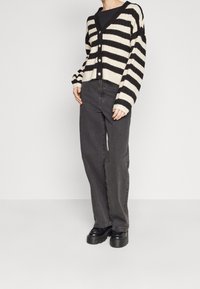 Czarny i kremowy kardigan w paski z dekoltem w serek, zapinany na guziki z prążkowaną fakturą, zestawiony z ciemnymi wysokim stanem jeansami i botkami na platformie.