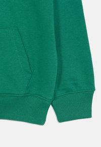 Zelená mikina s kapucňou s textúrovaným povrchom má klokanie vrecko a ribbené manžety. Materiál vyzerá mäkko a elasticky.
