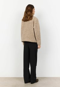 Beige, tekstureret, oversized sweater med rund halsudskæring, båret over høj talje sorte bukser med lige, brede ben.