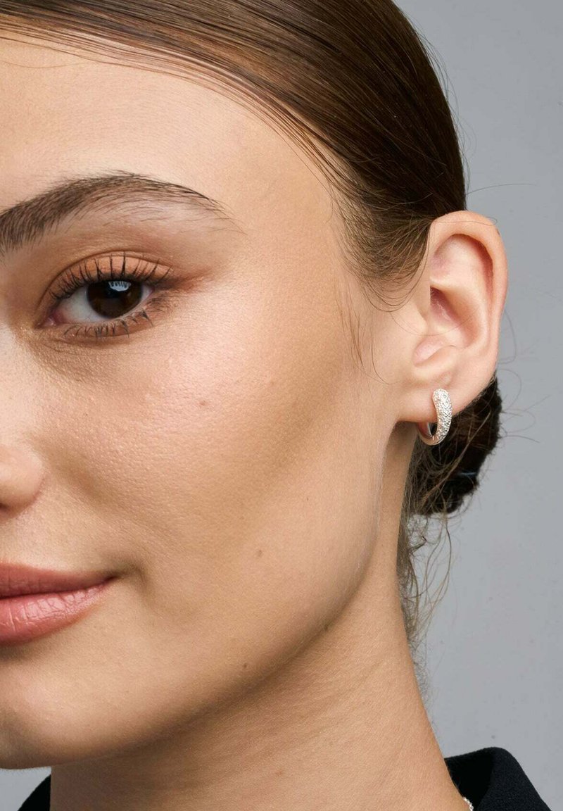 Orecchino a cerchio in argento con una superficie testurizzata, posizionato su un tono di pelle liscio, visto da vicino sull'orecchio di un modello.