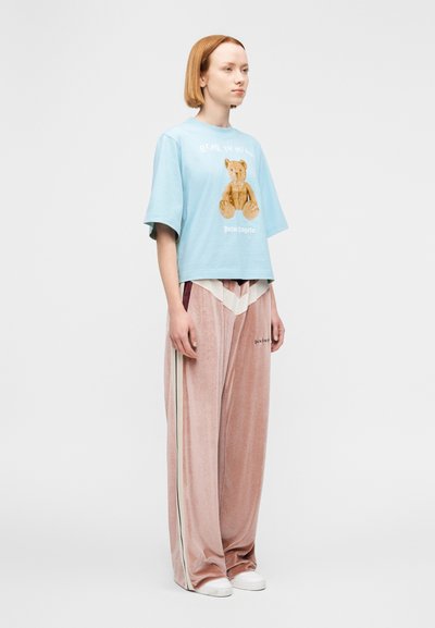 Ανοιχτό μπλε crop top με γραφικό αρκουδάκι και το κείμενο "Palm Angels", συνδυασμένο με απαλό ροζ βελουτέ παντελόνι με πλαϊνές ρίγες και λογότυπα.