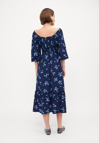 Mørkeblå blomsterkjole med off-shoulder halsutskjæring, trekvartlange ermer og volangkant. Laget av lett stoff med en glatt tekstur.