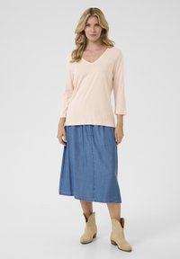 Hellrosa, langärmliges V-Ausschnitt-Oberteil kombiniert mit einem Denim-Maxirock; beige Cowboystiefel vervollständigen das Outfit. Glattes Material mit subtiler Textur.