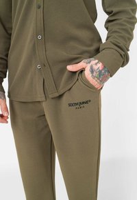 Fleece loungewear set in olive green. Button-up shirt with textured fabric, side pockets, and logo detail on pants.