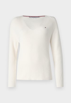 Crème-kleurige v-hals trui, geribbeld patroon, lange mouwen, met een klein logo accent op de borst. Gemaakt van zacht breimateriaal.