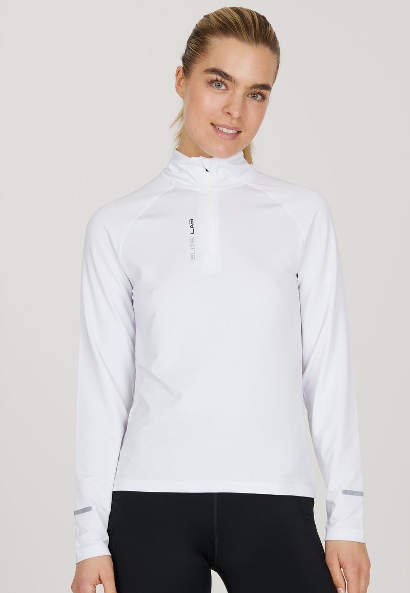 Weißes langärmliges Sportoberteil mit einem halben Reißverschluss, aus weichem Stoff, reflektierendem Logo und grauen Akzenten an den Bündchen, getragen zu schwarzen Leggings.