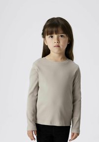 Hellbeige langärmliges, geripptes Oberteil mit rundem Ausschnitt, kombiniert mit schwarzen Hosen. Weiche Textur, figurbetontes Design und minimale Details.