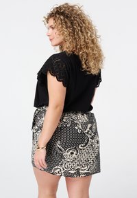Haut noir avec des détails en dentelle sur les manches, associé à une jupe à motifs présentant des designs floraux et géométriques en crème et noir.