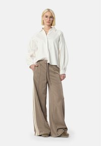 White, long-sleeve button-up shirt with voluminous sleeves paired with beige, wide-leg sweatpants featuring side stripes and drawstring waist.