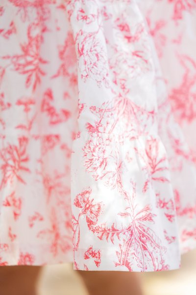 Vestido branco com padrão floral em rosa, apresentando um acabamento franzido ao longo da barra e um tecido macio e leve com uma textura suave.