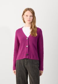 V-neck, purple knit cardigan with ribbed texture, three buttons at the front, long sleeves, and a cropped hem. Paired with a white shirt.