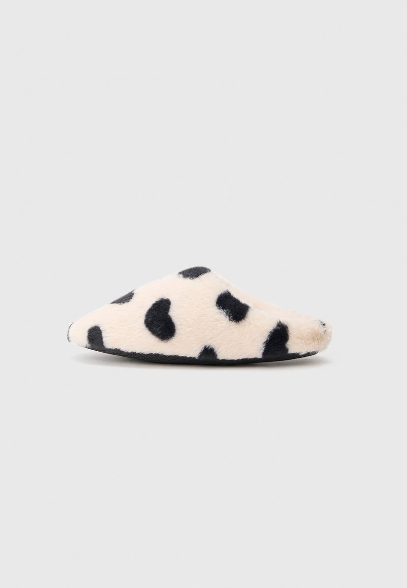 Pantufa suave e felpuda em bege com padrão de vaca preto. Apresenta um bico pontiagudo e design de calçar, com sola preta. Adequada para uso interior.