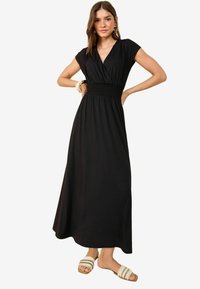 Rochie maxi neagră cu decolteu în V, mâneci scurte și talie elastică. Material neted cu un design fluid. Asortată cu sandale cu curea.