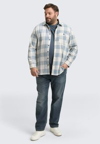 Flanellen overhemd in lichtblauw en wit ruitpatroon, gedragen over een donkerblauw t-shirt. Denim jeans met een relaxte pasvorm en witte sneakers.
