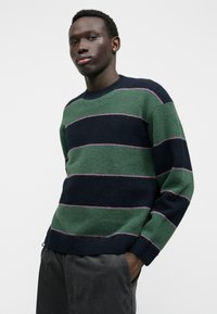 Maglione a righe verdi e blu navy con accenti rosa, realizzato in materiale a maglia testurizzata e caratterizzato da un collo a giro e polsini a costina.