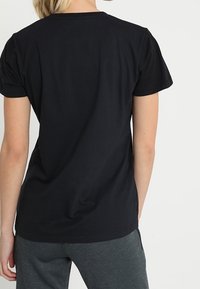 Camiseta de algodón negra, de manga corta, con cuello redondo, textura suave, ajustada en los hombros, ligeramente holgada en el torso, diseño liso.