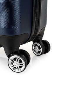 Maleta rígida de color azul marino con una superficie texturizada, que cuenta con un cierre negro y cuatro ruedas giratorias multidireccionales con detalles en platino.