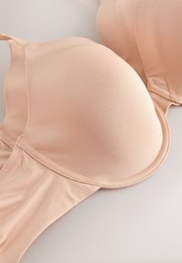 Soutien-gorge nude lisse et rembourré avec armature et bretelles ajustables, posé à plat sur une surface claire, montrant les détails de la coque et de la bande.