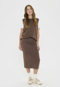 Rjava pletena dvodelna obleka, ki vključuje brezrokavni top in ujemajočo se midi krilo. Obuta s kremnimi nogavicami in bež supergami.