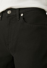 Jeans in denim nero con una trama liscia, caratterizzati da un bottone argentato e cuciture a contrasto, e un classico design a cinque tasche.