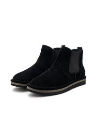 Stivali alla caviglia neri in suede con pannelli laterali elastici, suola in gomma e design piatto. Presentano una striscia marrone a contrasto lungo la suola.