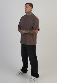 Rjava kratka majica s kratkimi rokavi, bombažni material, sproščen kroj. V kombinaciji z črnimi širokimi hlačami in belimi/sivimi supergami. Enostaven dizajn, brez vzorcev.