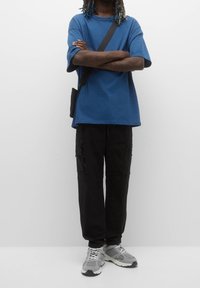 Blaues übergroßes T-Shirt, schwarze Cargo-Hosen mit mehreren Taschen und graue Sneakers. Das Outfit hat eine lässige, entspannte Passform mit kurzen Ärmeln.