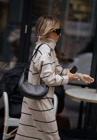 Abito maglione beige con righe nere, colletto alto e vestibilità ampia; abbinato a una borsa a spalla nera. Accessorio: occhiali da sole neri oversize.