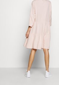 Abito rosa a strati con maniche a tre quarti, caratterizzato da una vestibilità ampia e una consistenza morbida, indossato con sneakers bianche. Design semplice, senza fantasie.