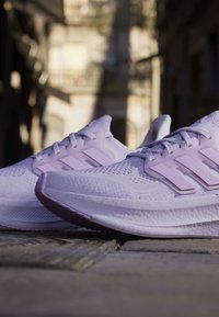 Двойка светлолилави маратонки Adidas на калдъръмена улица с размит градски фон на дневна светлина.