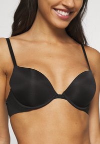 Zwarte push-up beha met gladde, gevormde cups, verstelbare bandjes en een banddetail met textuur. Eenvoudig ontwerp zonder versieringen.