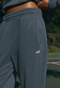 Grijze katoenen sweatpants met een relaxte pasvorm, elastische tailleband, zijzakken en een klein wit "self." logo op de linkerdij.