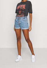 Camiseta gráfica negra con el texto "BIGGIE", combinada con pantalones cortos de mezclilla azul claro que tienen una cintura fruncida y cinco botones. Zapatillas blancas.