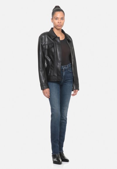 Giacca in similpelle nera con un design a colletto e due tasche frontali, abbinata a jeans in denim scuro a vita alta e stivali alla caviglia.