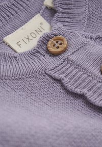 Eine lila gestrickte Sweatshirt mit einem gerippten Kragen, einem Holzknopf und strukturiertem Stoff. Das Etikett trägt die Aufschrift "FIXONI." Nahaufnahme.