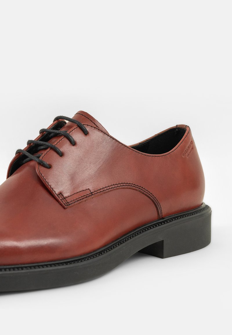 Brązowe skórzane buty eleganckie z czarnymi sznurowadłami, z zaokrąglonym noskiem i grubą czarną gumową podeszwą; gładka tekstura z subtelnymi detalami w szyciu.