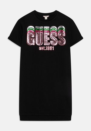 Vestido negro de manga corta con gran logo GUESS de lentejuelas en plata, verde y rojo, y texto más pequeño "est. 1981" debajo en el pecho.