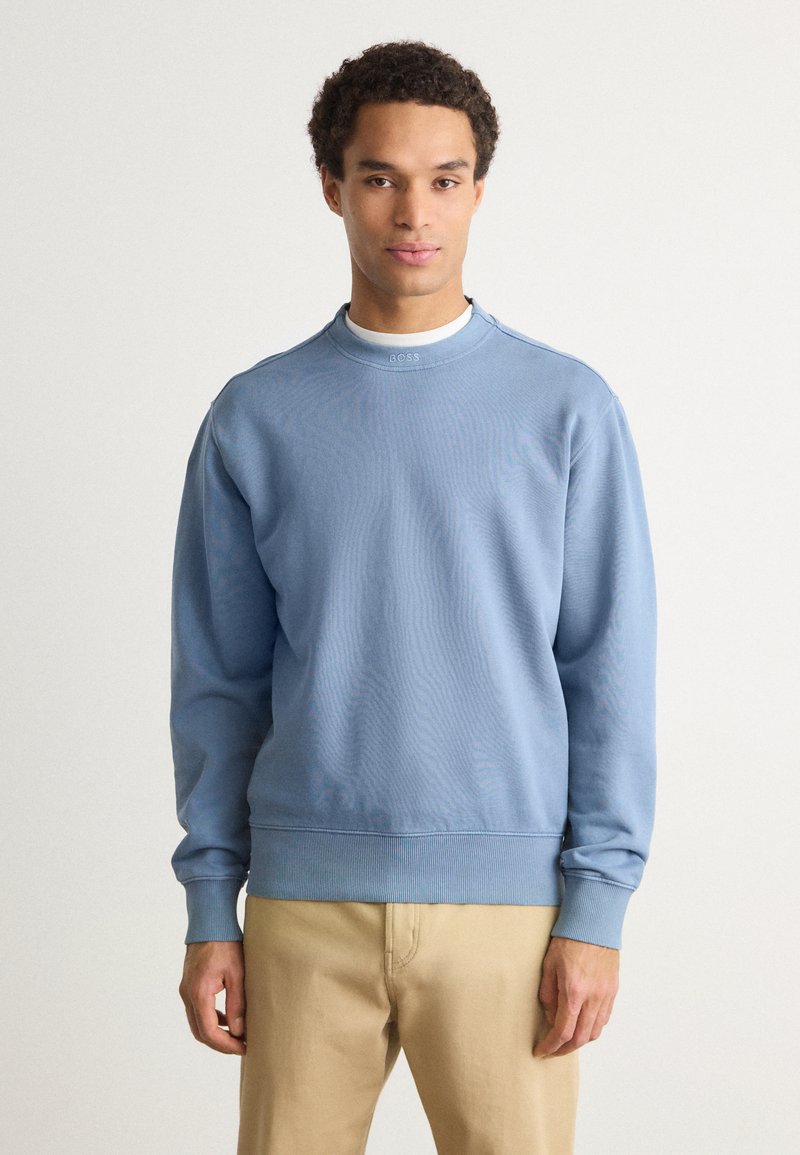 Ανοιχτό μπλε φούτερ με ριμπ λαιμόκοψη, μακριά μανίκια και εφαρμοστό τελείωμα. Διαθέτει διακριτικό λογότυπο κοντά στον λαιμό και μαλακή υφή.