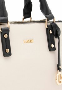 Sac structuré en simili cuir crème et noir. Présente des accessoires en or, des poignées doubles et un logo décoratif. Fermeture zippée.