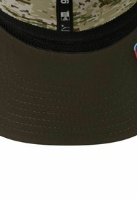 Dunkelgrüne Kappe mit flachem Schild und strukturiertem Innenfutter. Sie hat ein Camouflage-Muster auf der Innenseite und kontrastierende Nähte. Dekoratives Abzeichen enthalten.