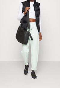 Svart pufferväst över en vit crop top, kombinerat med mintgröna joggers och svarta sneakers. En svart axelväska hänger från armen.